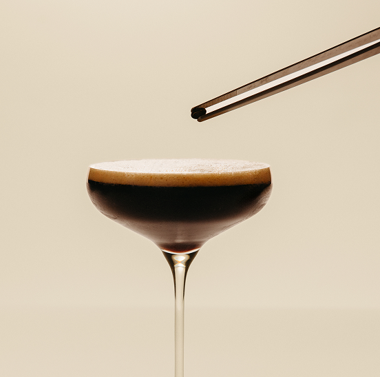 Zero proof Dry and Dirty espresso martini in a glass with a thin layer of foam on a beige background